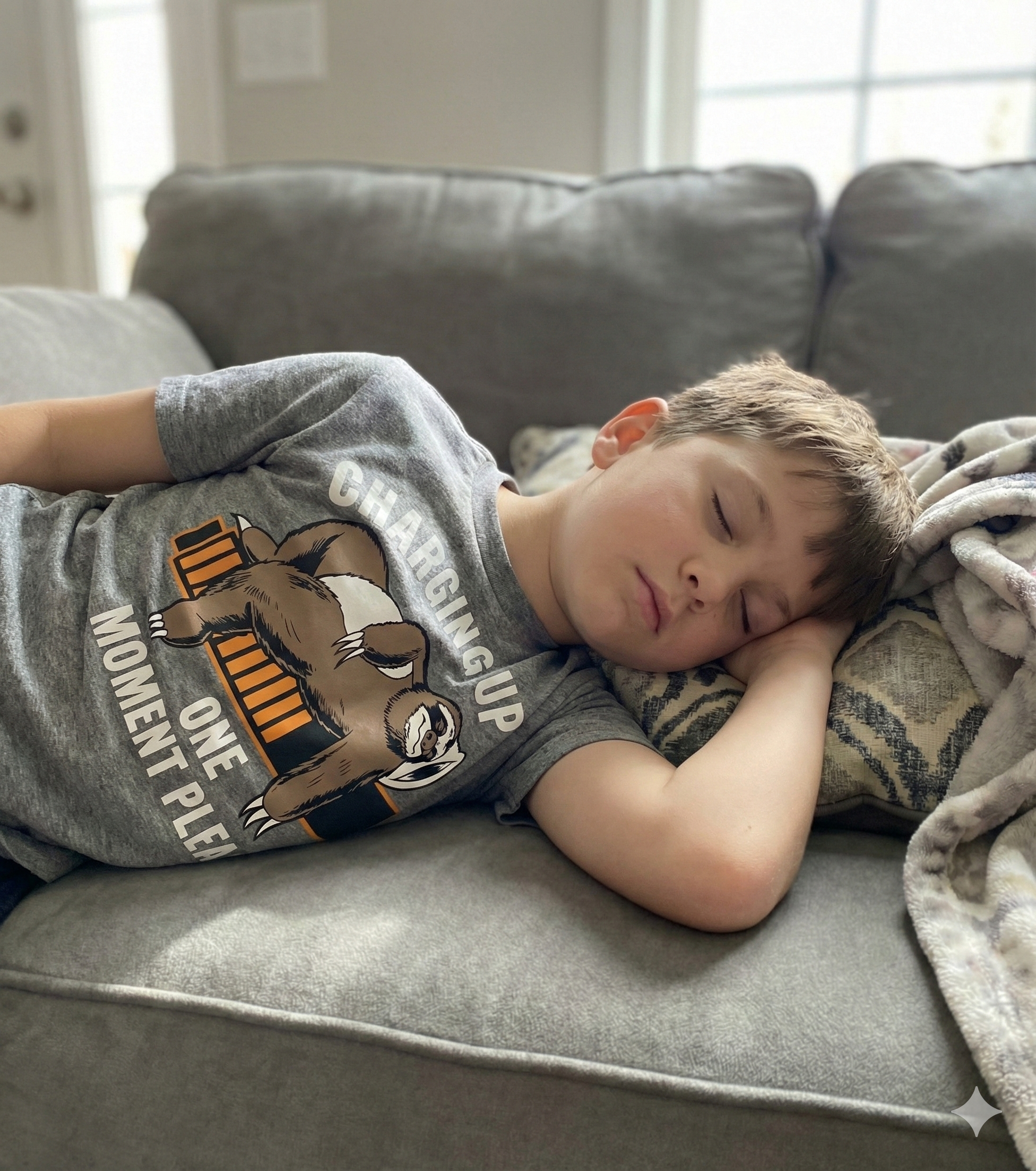 Child sleeping on a couch wearing a gray t-shirt with a bear graphic and text.