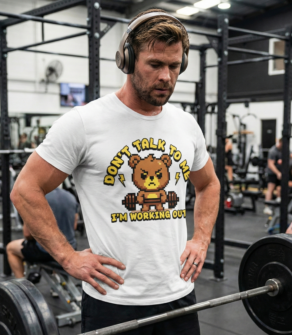 Man in a gym wearing a white t-shirt with a bear graphic and text, surrounded by gym equipment.